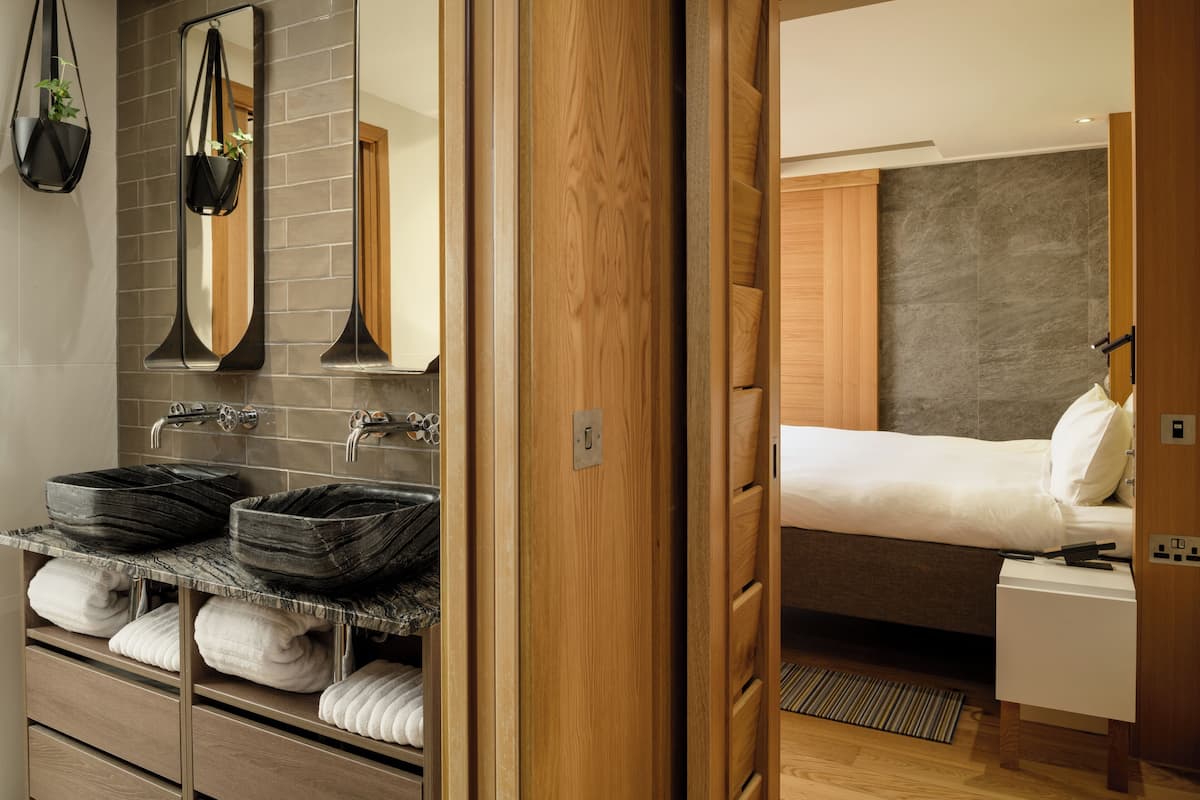 A modern bathroom with a large mirror, two black marble sinks, and a wooden vanity.