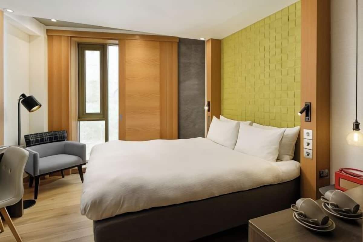 A hotel room with a large bed, a desk with a chair, a sofa, and a window.