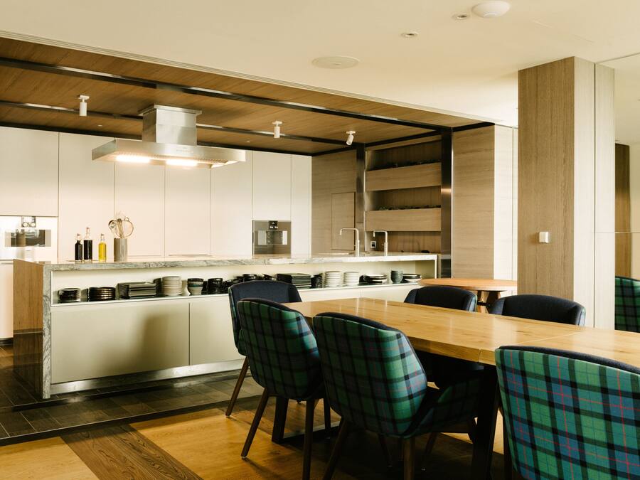 A modern kitchen with a central island, white cabinetry, and a dining area with plaid chairs.