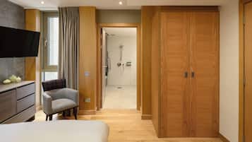 A modern hotel room with a large bed, a flat-screen TV, a wooden wardrobe, and a shower area.