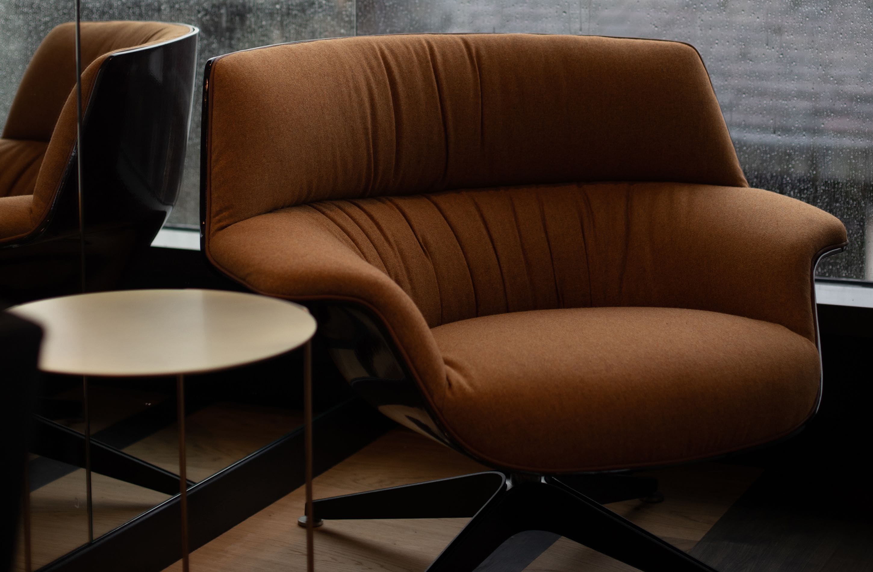 Une pièce moderne avec un fauteuil à revêtement marron, une petite table ronde et une chaise noire.