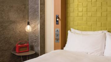Une chambre d’hôtel avec un lit, une table de chevet sur laquelle se trouve une radio rouge, un luminaire et un mur orné d’un panneau texturé.