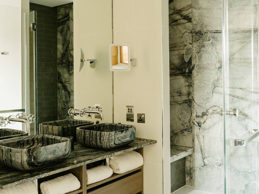 A bathroom with three large, marble-like sinks, a glass-enclosed shower, and a mirror above the sinks.