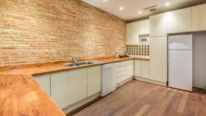 Una cocina con pared de ladrillo, encimera de madera, armarios blancos, lavavajillas, microondas y refrigerador.