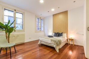 A bedroom with a bed, a chair, a bedside table, a lamp, and a radiator.