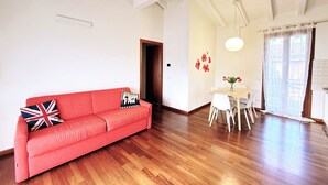 A spacious room with a red sofa, white chairs, a wooden dining table, and a large window with sheer curtains. - Il Papavero apartment Sirmione | Terme & Garda Lake (Sirmione)