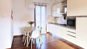 A modern kitchen with white cabinets, a built-in oven, and a dining area with a wooden table and chairs. - Il Papavero apartment Sirmione | Terme & Garda Lake (Sirmione)