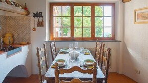 A dining room with a wooden table set for four, a window with a view of greenery, and rustic decor including a lantern and a shelf with kitchen items. - Santa Lucia Suite, Lovely View Over the Shore.. (Camaiore)