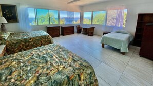 A spacious bedroom with two beds, a ceiling fan, and large windows offering a view of the outdoors.