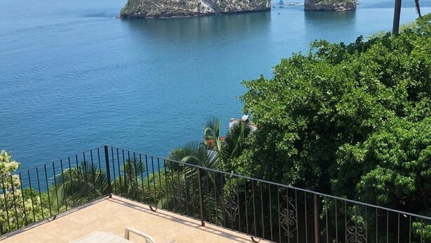 A terrace with a pool, lounge chairs, and a view of the sea and islands.