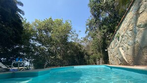 A clear blue pool surrounded by lush greenery and a stone wall.