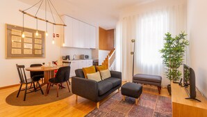 A modern living room with a sofa, ottoman, and coffee table, a dining area with chairs and a table, and a kitchen in the background. - Very Nice Decorated 2 Bedroom Apartment (Oporto)