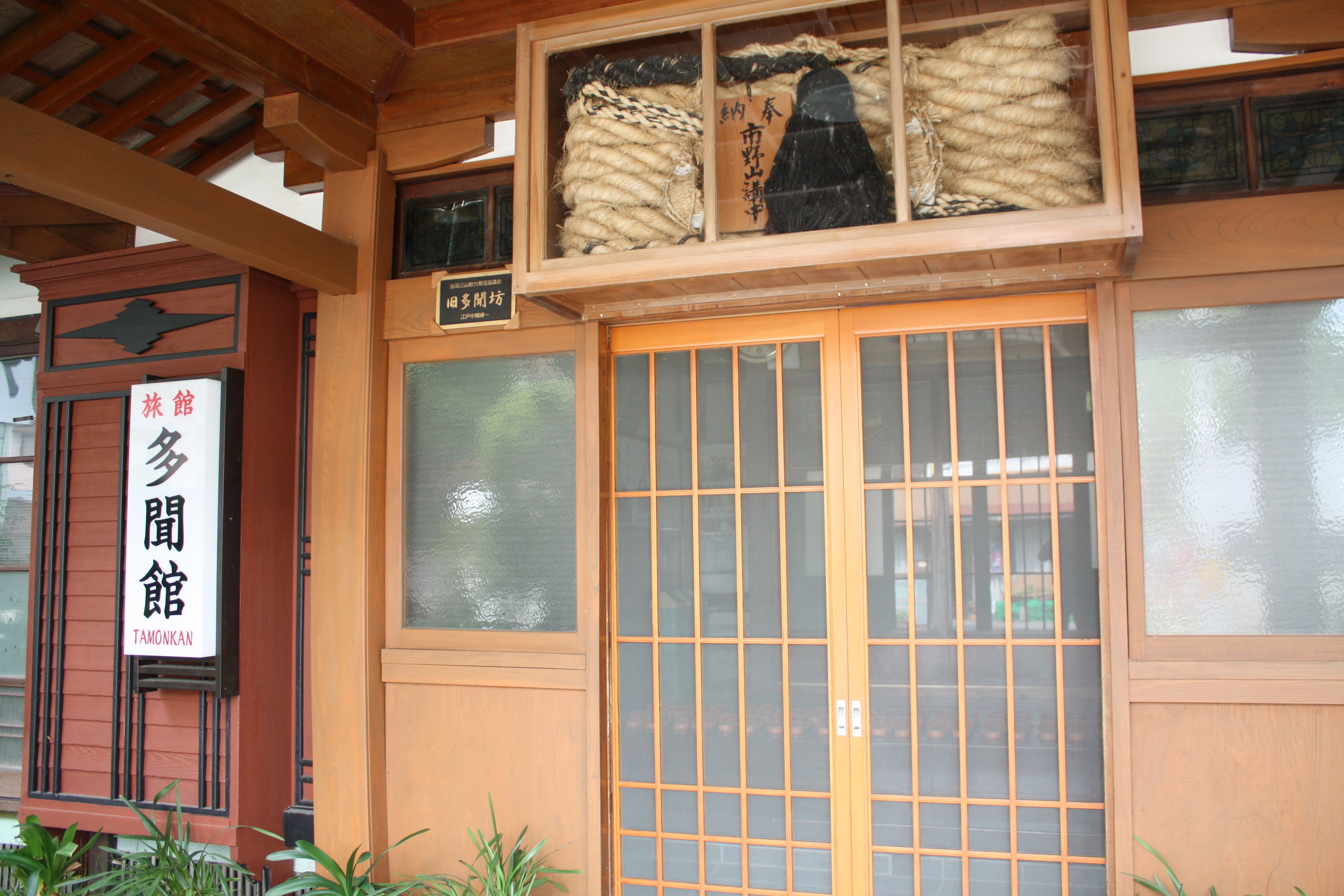 Il s’agit d’un bâtiment japonais traditionnel, avec une façade en bois, une grande porte coulissante dotée de panneaux de verre et une enseigne indiquant qu’il s’agit d’un « Tamokan ».