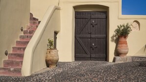 A building with a beige exterior, a dark wooden door, and a staircase leading to the entrance. - Mansion Kyani- Spectacular Santorini villa- Car included- Private & Spacious (Santorini)