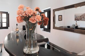 A clear glass vase with flowers on a black countertop, a mirror on the wall, and a framed picture above it. - Mansion Kyani- Spectacular Santorini villa- Car included- Private & Spacious (Santorini)