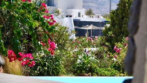 A view of a building with a white facade and a blue roof, surrounded by lush greenery and pink flowers. - Mansion Kyani- Spectacular Santorini villa- Car included- Private & Spacious (Santorini)