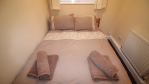 A single bed with a beige duvet and two pillows, a radiator on the right, and a window with curtains.