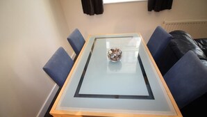 A dining area with a glass-top table, four blue chairs, and a bowl of snacks on the table.