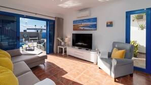A living room with a sofa, a TV, and a balcony with outdoor furniture. - Air-conditioned Villa With Mountain Views, 300m From Coastal Path - Villa Elise (playa blanca)