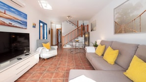 A living room with a TV, sofa, and chairs, a staircase, and a dining area. - Air-conditioned Villa With Mountain Views, 300m From Coastal Path - Villa Elise (playa blanca)