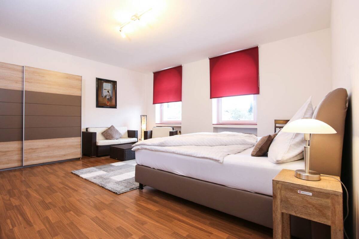 A modern bedroom with a large bed, a bedside table with a lamp, a wooden floor, and a sliding door closet.