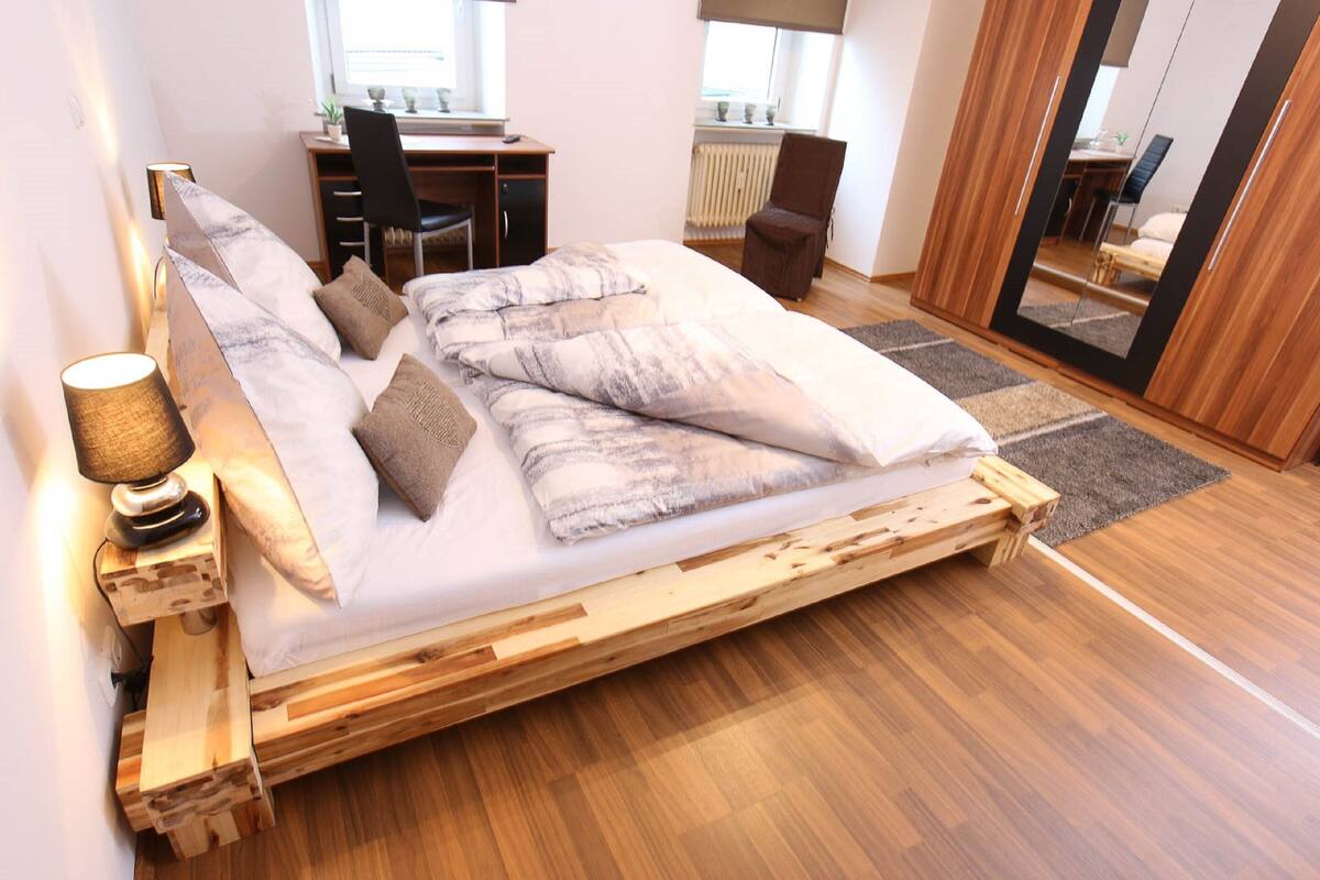 A bedroom with a wooden bed, a desk, a chair, and a mirror.