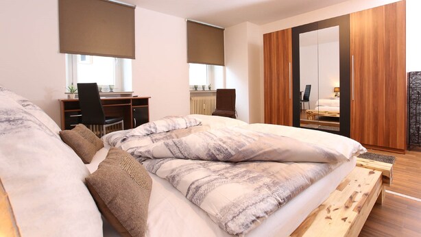 A bedroom with a bed, a desk, and a wardrobe. - Pension Leonardo (Aidenbach)
