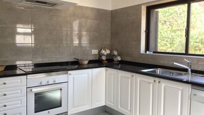 A modern kitchen with white cabinets, a black countertop, a built-in oven, and a window with a view of greenery. - Casa dos Caes - Private pool, just 500m from golf course & 1.5km from beach (Carvoeiro)