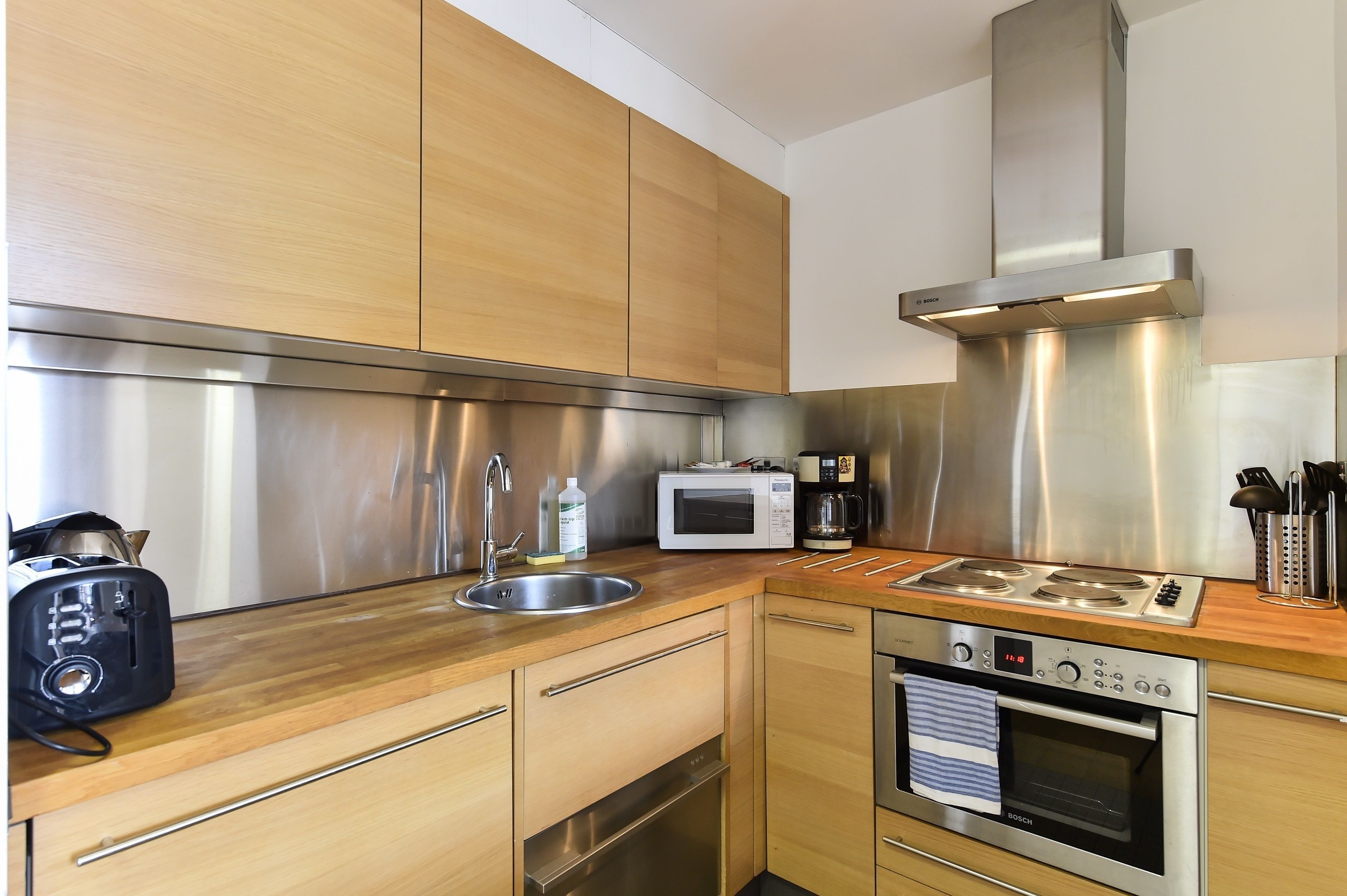Eine moderne Küche mit Holzschränken, Edelstahlgeräten, einer Spüle, einem Toaster, einer Mikrowelle, einer Kaffeemaschine und einem Backofen.