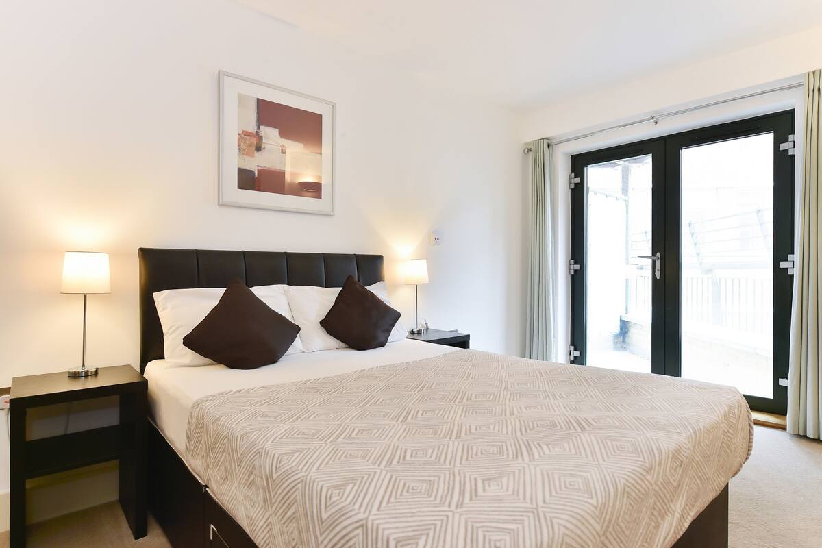 A hotel room with a large bed, two bedside lamps, a framed picture on the wall, and a sliding glass door to the outside.