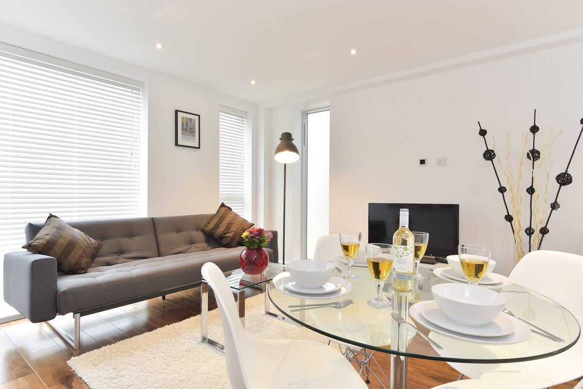 A modern living room with a glass dining table set for two, a sofa, and a fireplace.