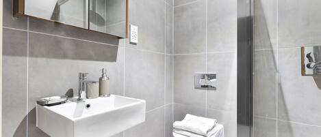 A modern bathroom with a white sink, a toilet, and a glass shower enclosure.