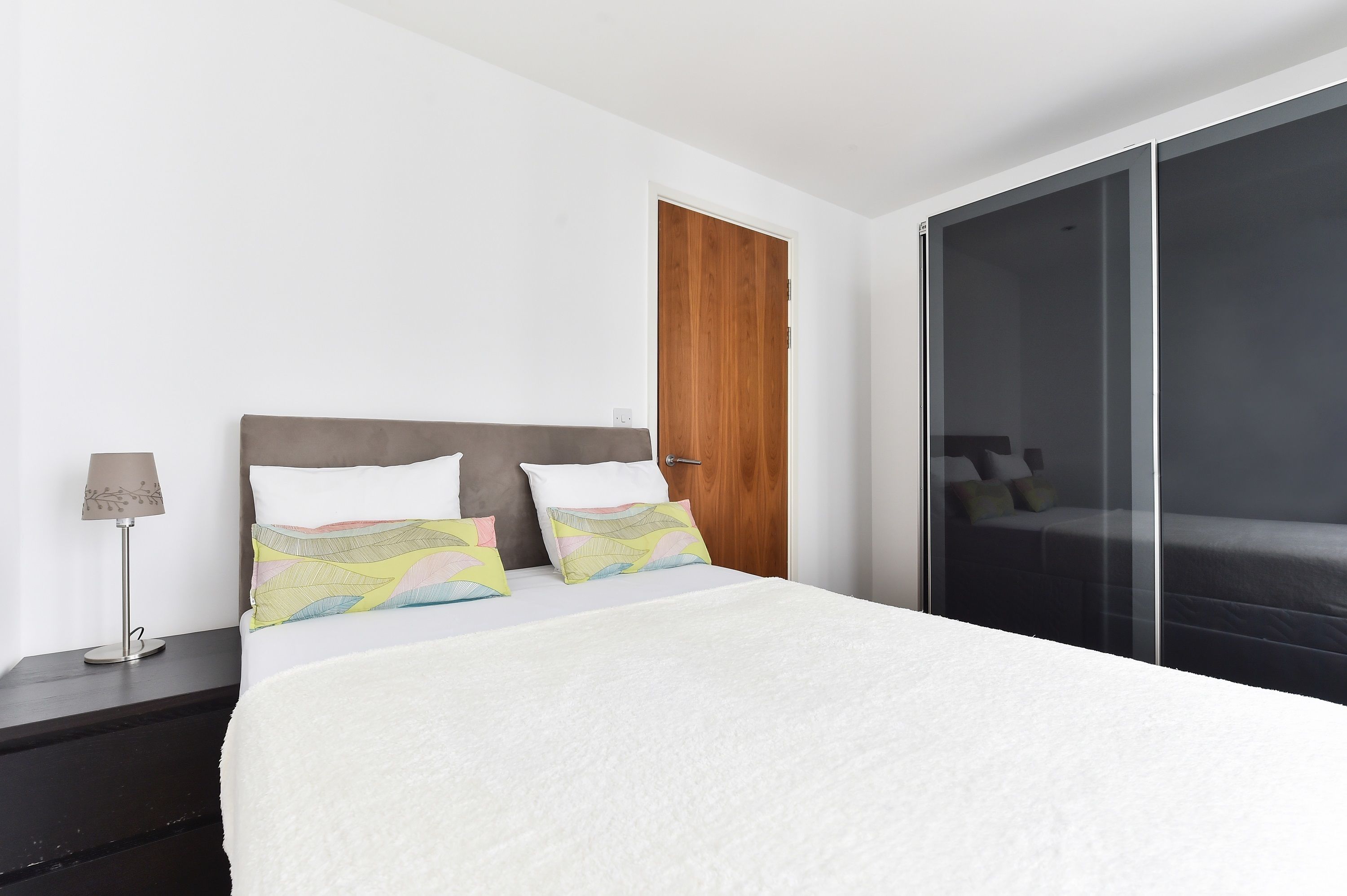 A modern hotel room with a large bed, a wooden door, and a sliding glass door leading to a balcony.