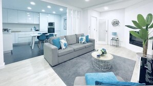 Ein modernes Wohnzimmer mit einem grauen Sofa, einem Couchtisch und einem Essbereich im Hintergrund.