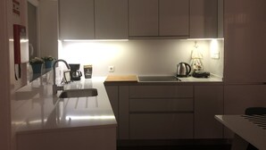 Eine moderne Küche mit weißen Schränken, einer Edelstahl-Spüle, einer Kaffeemaschine und einem Wasserkocher.
