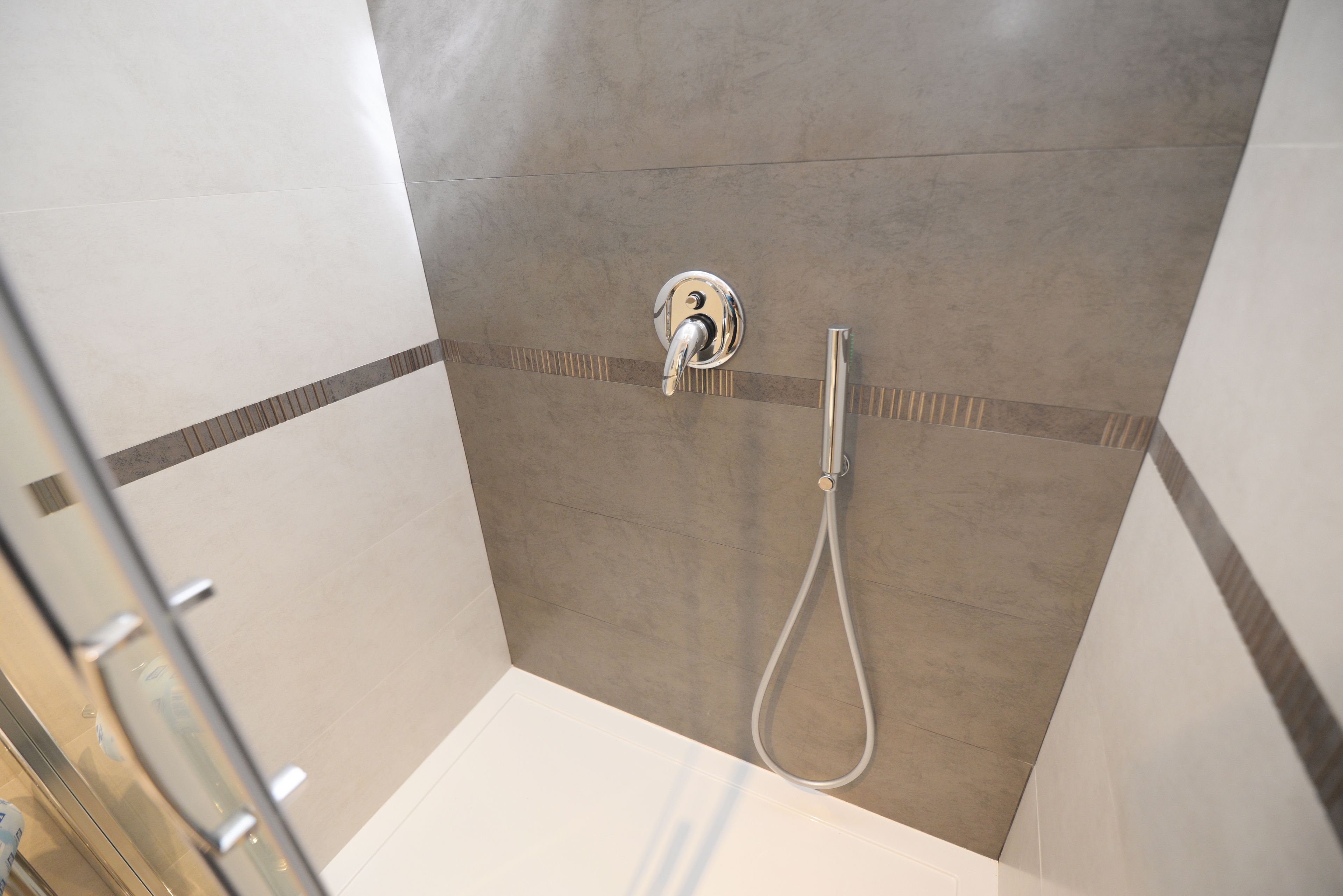 A shower with a handheld showerhead and a wall-mounted faucet.