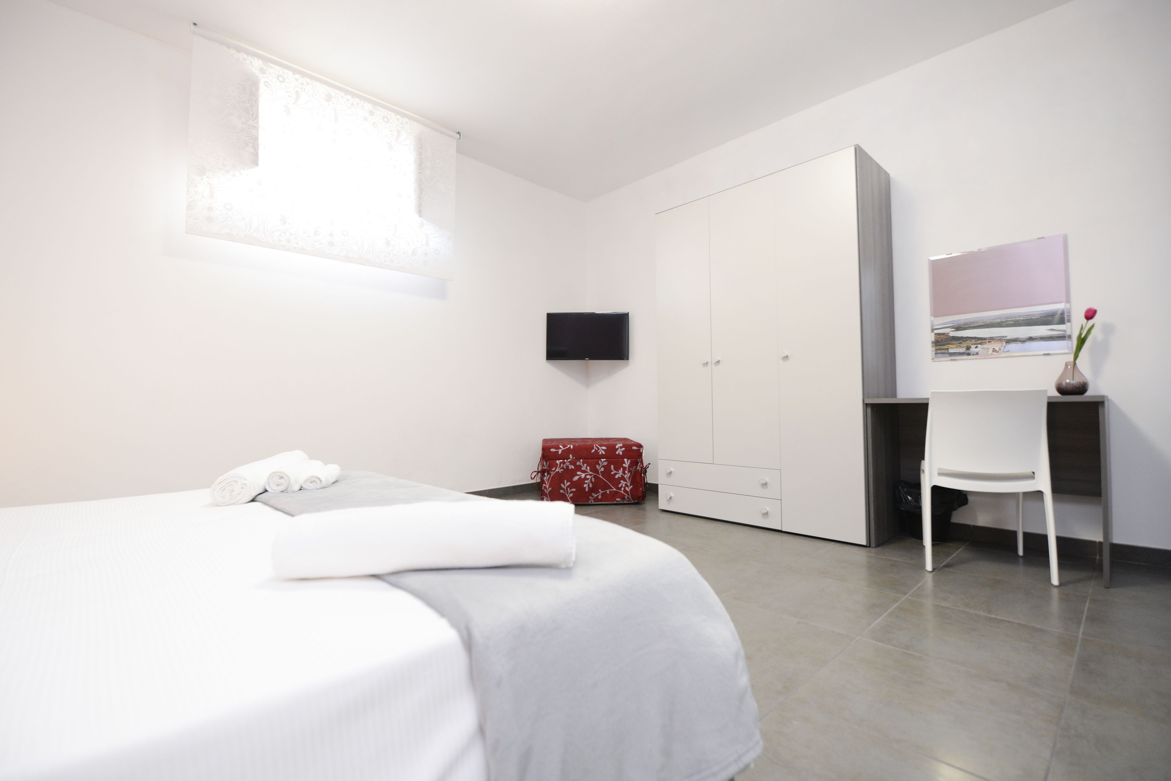 A modern bedroom with a bed, a TV, a wardrobe, and a desk with a chair.