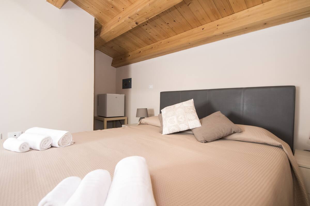 Een net opgemaakt bed met hoofdbord, kussens en opgerolde handdoeken.
