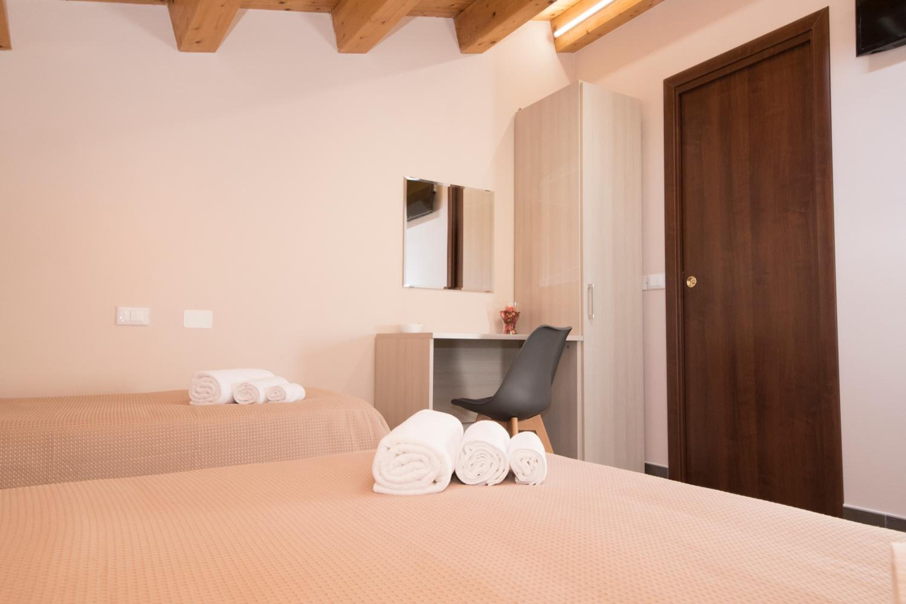 Una habitación de hotel con dos camas, un escritorio, una silla, un espejo y una puerta de madera.
