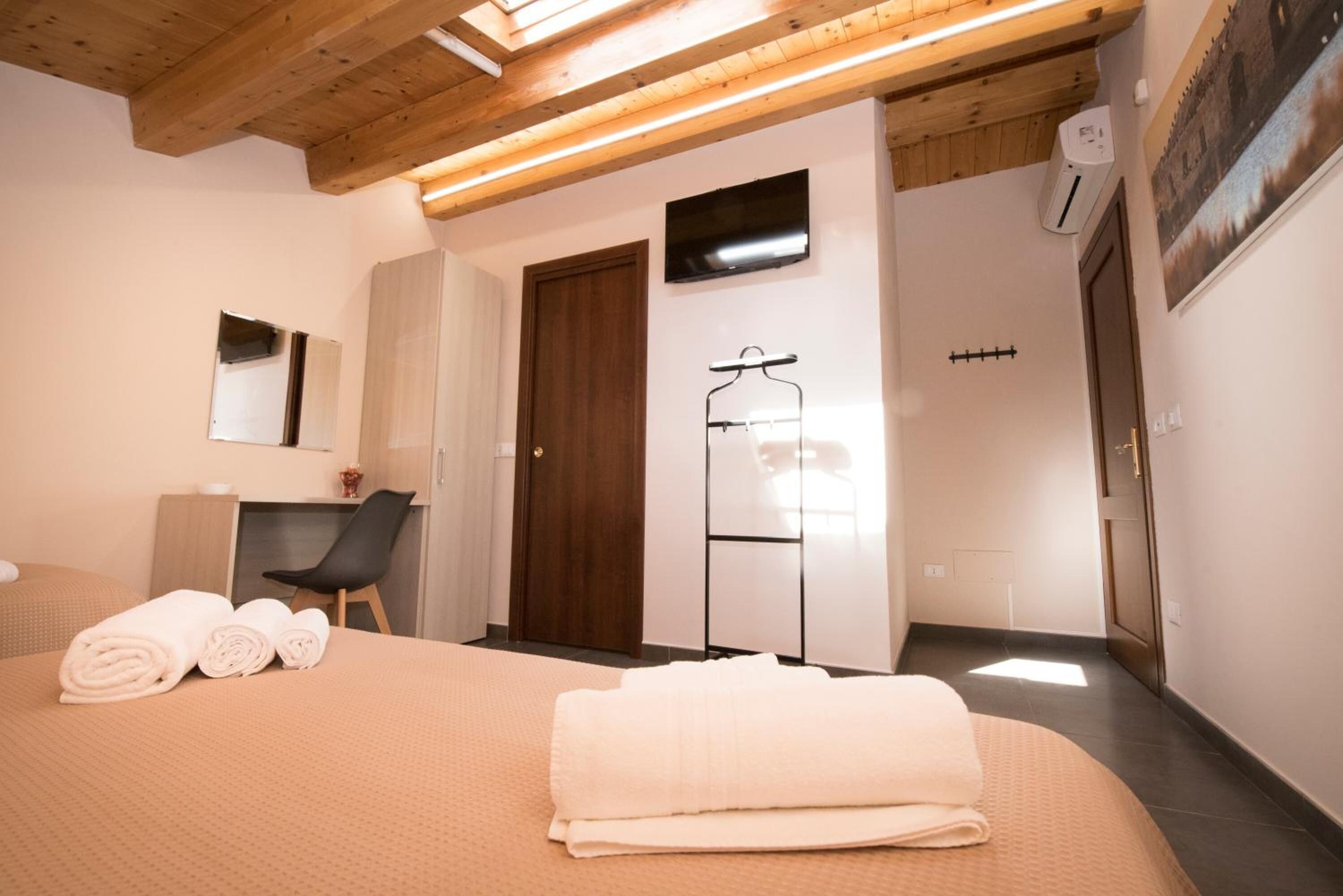 A hotel room with a bed, a desk, a chair, a wardrobe, a mirror, and a TV.