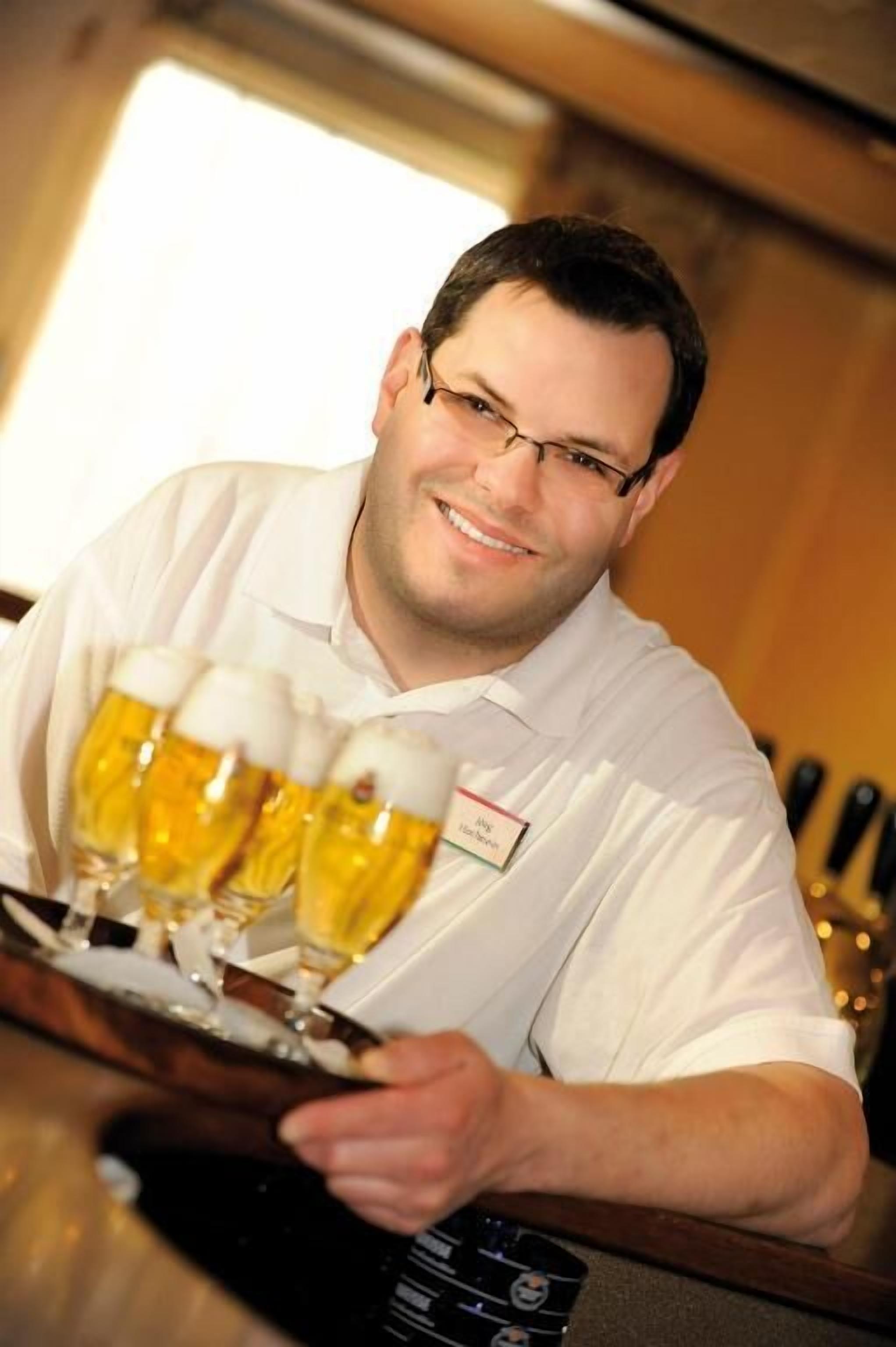 A person holding a tray with four glasses of beer.