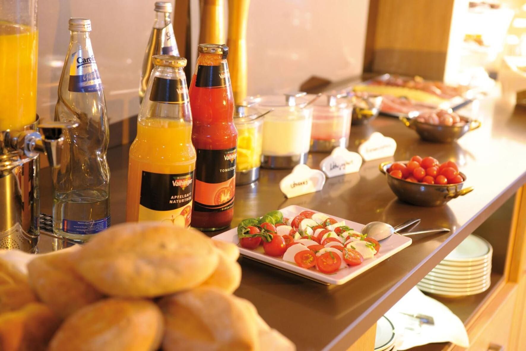 A buffet with various food items, including a plate of tomato and mozzarella salad, and several bottles of beverages.