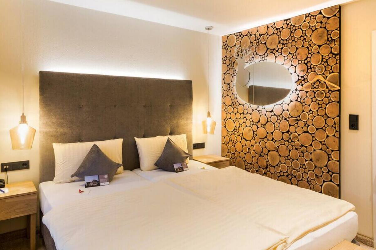 Quarto de hotel com uma cama grande, duas mesas de cabeceira, um espelho fixado na parede e um padrão circular de madeira na parede.