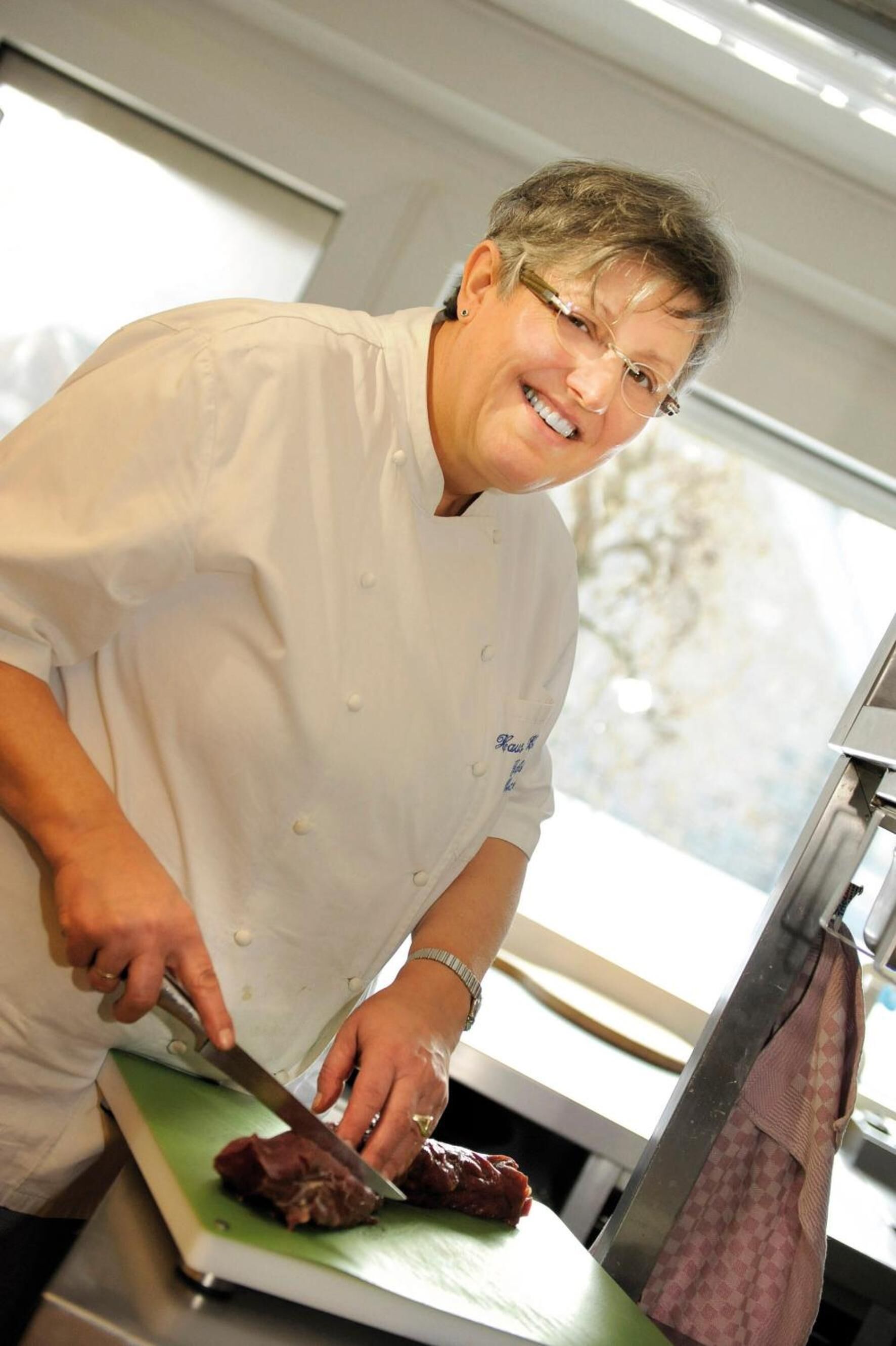 A chef cutting meat on a cutting board in a kitchen.