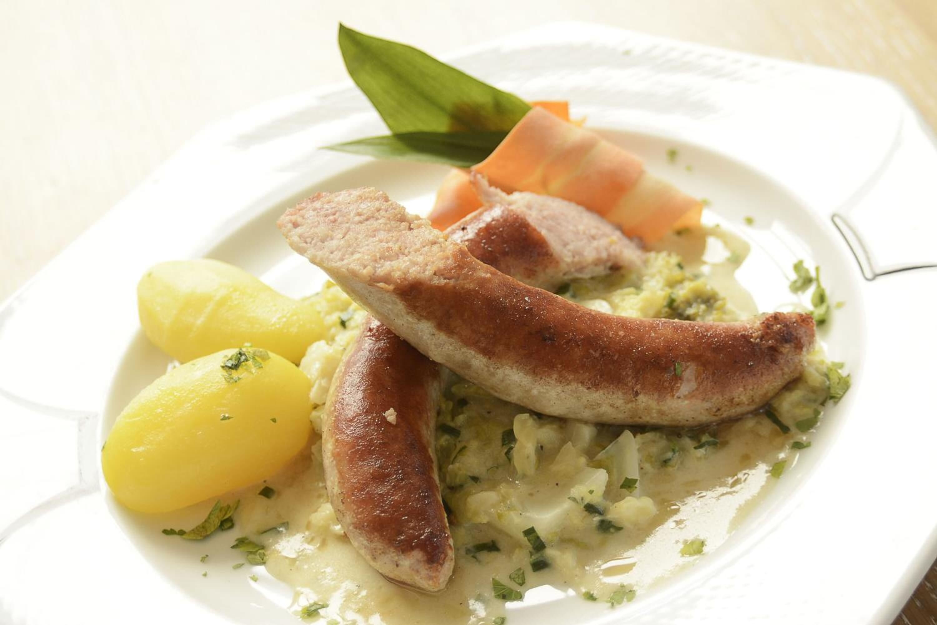 A plate with sausages, boiled potatoes, and a creamy sauce.