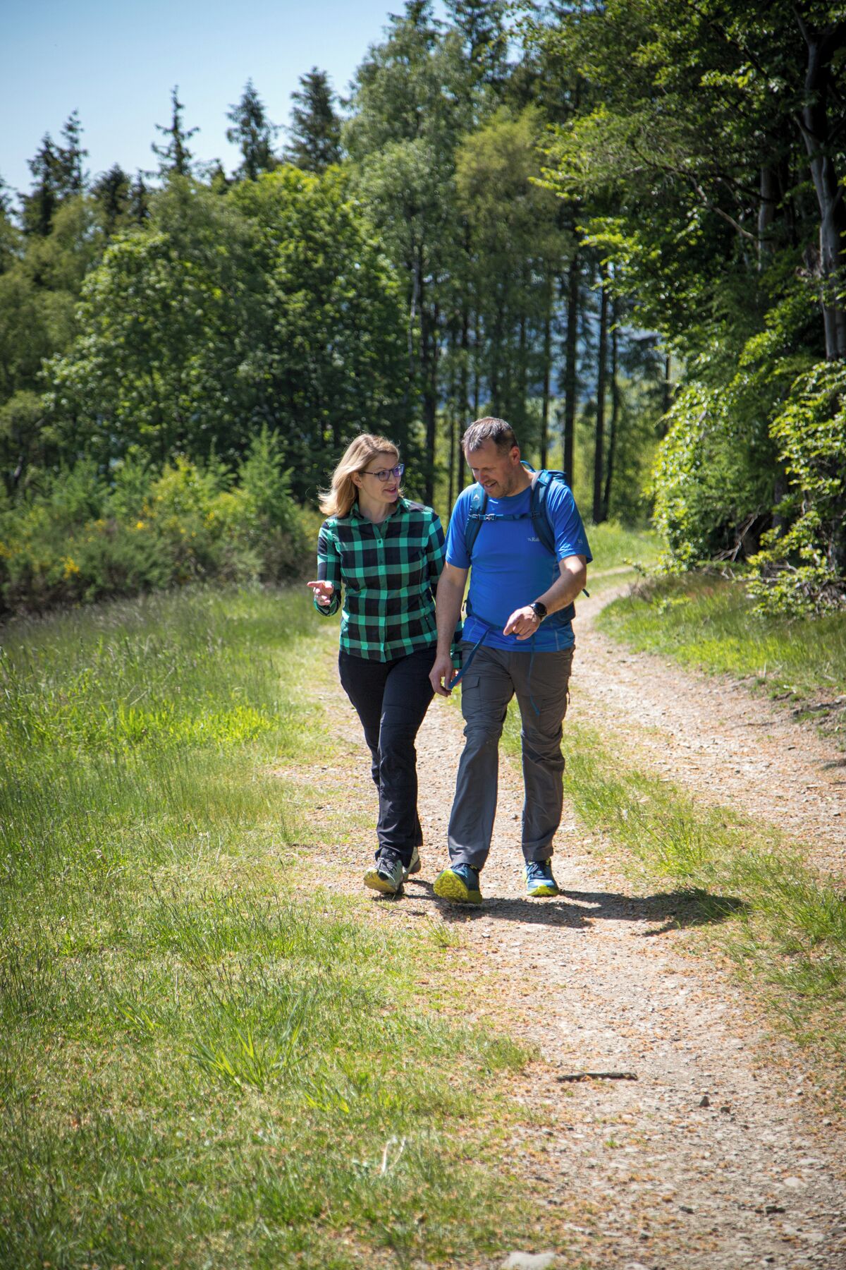 Two people walking on a gravel path surrounded by greenery.