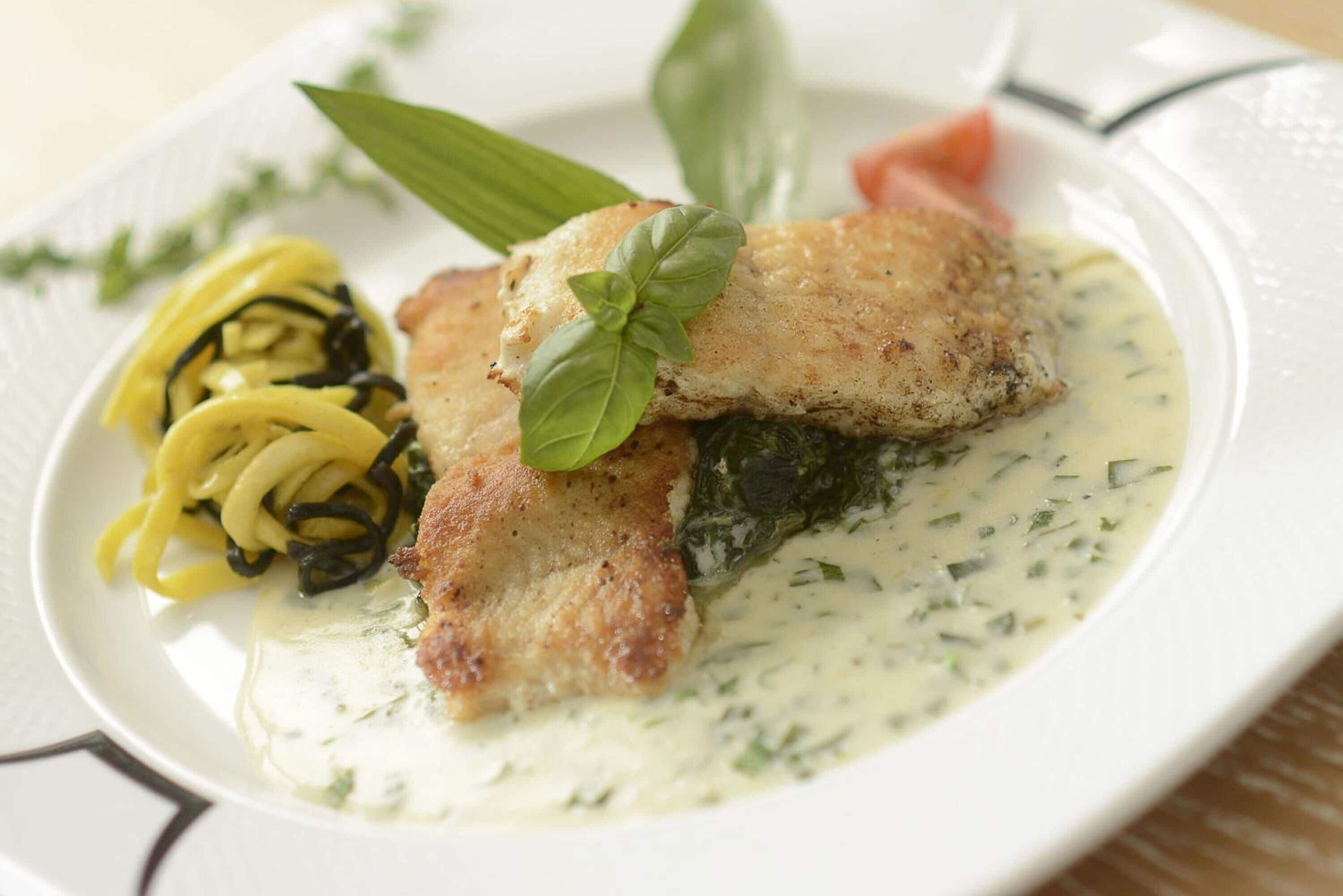 A plate of food with a fish fillet, pasta, and a creamy sauce.