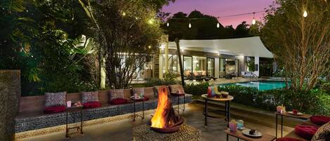 Zona junto a la piscina con un hogar, asientos al aire libre y vista a la casa.