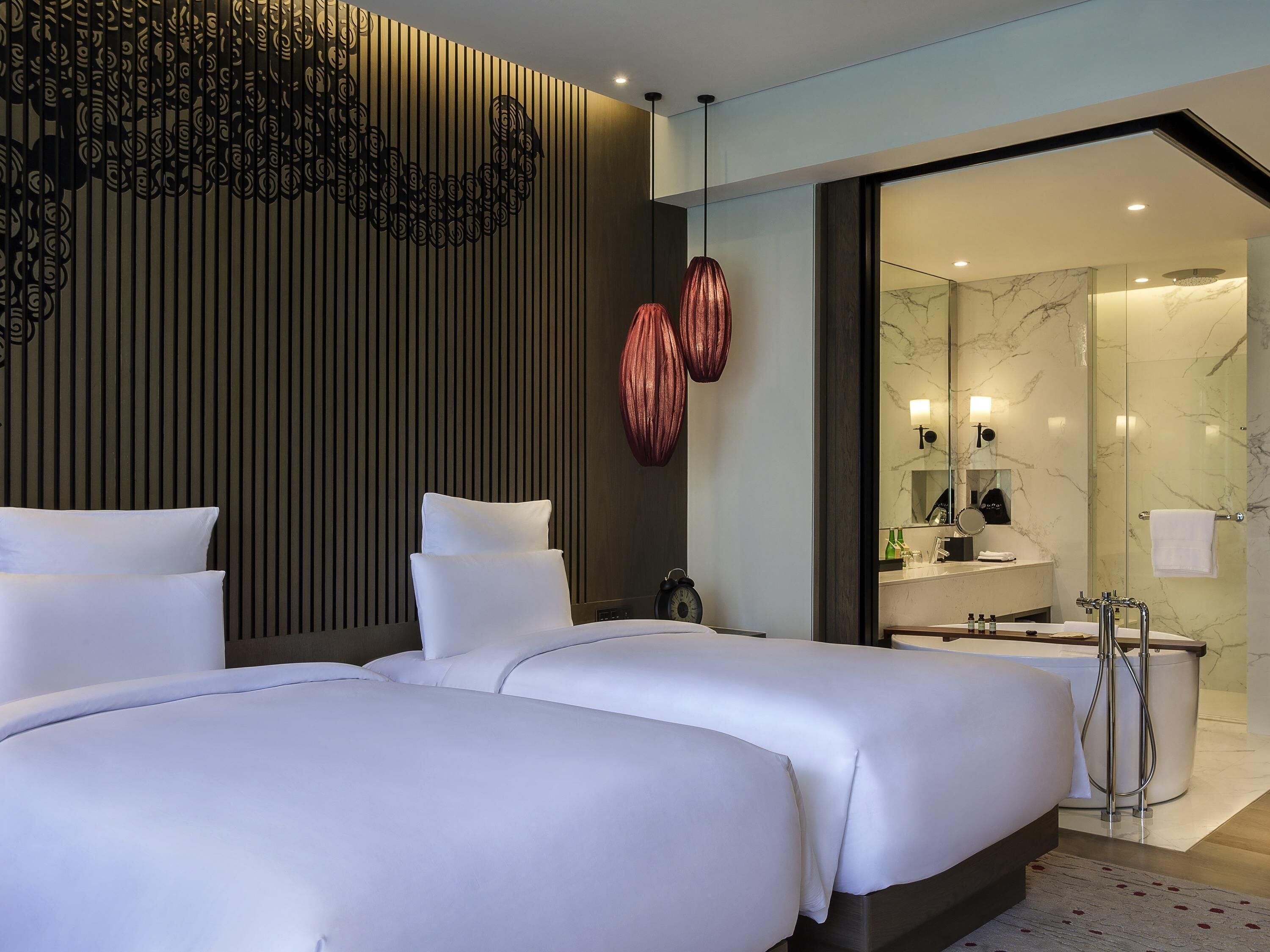 A hotel room with two beds, a modern bathroom with a glass shower, and a decorative wall panel.