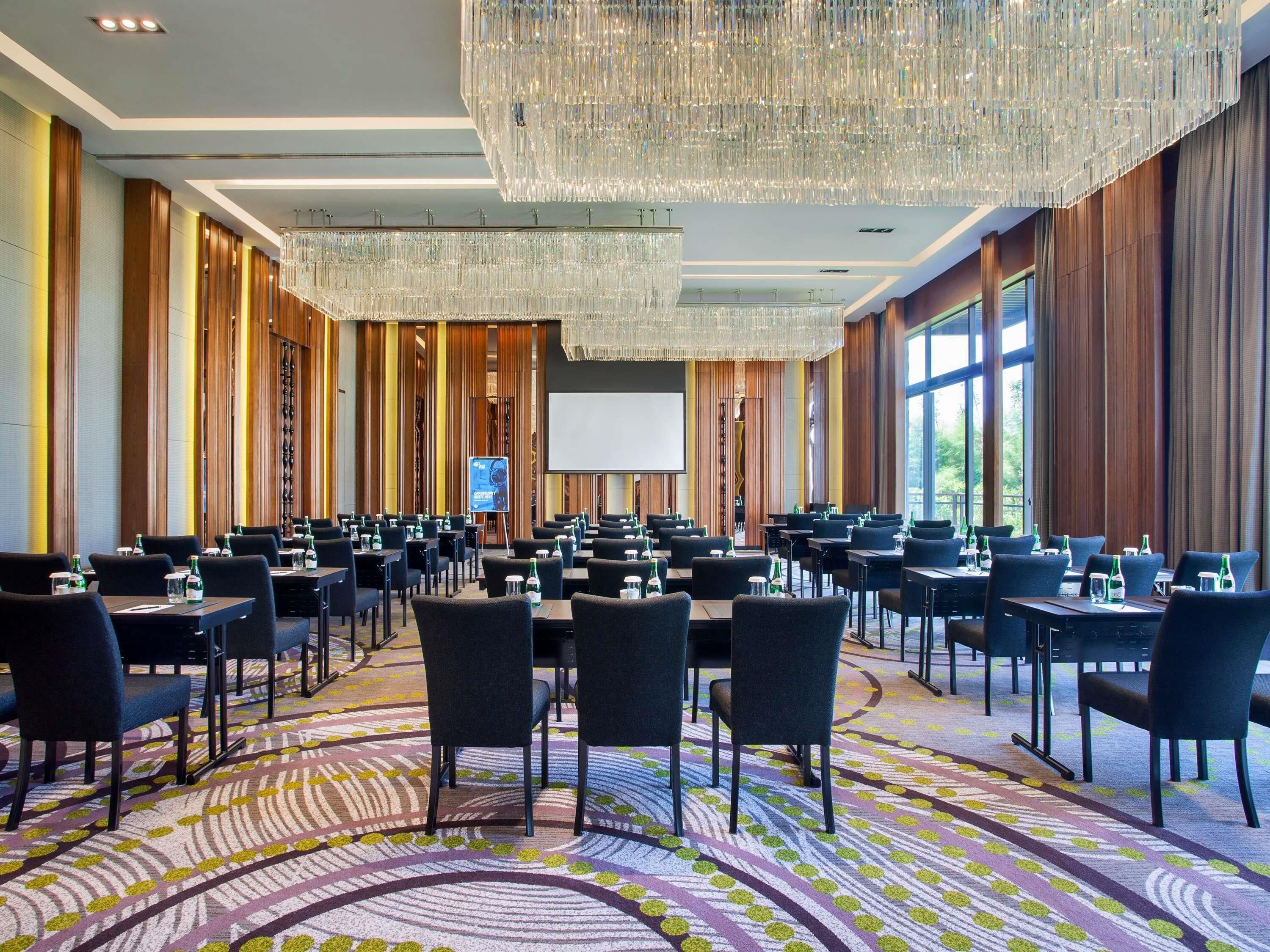A conference room with multiple tables and chairs, a large screen, and a patterned carpet.
